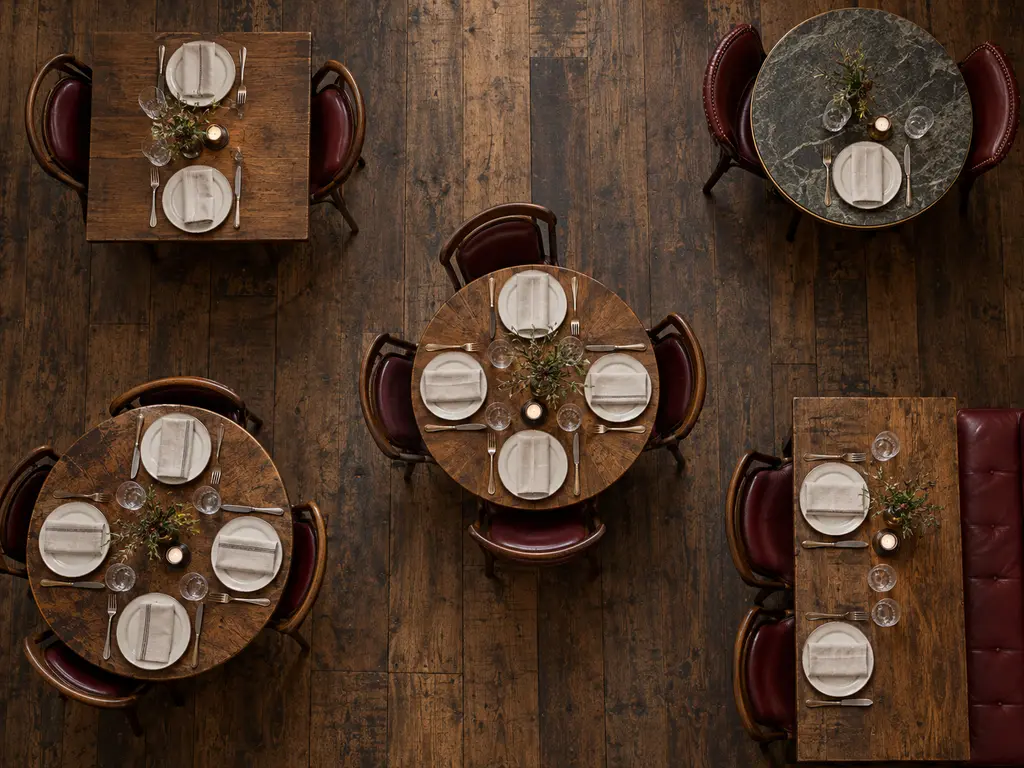 A dining room seen from directly above: round and square tables set with white plates on a dark wood floor